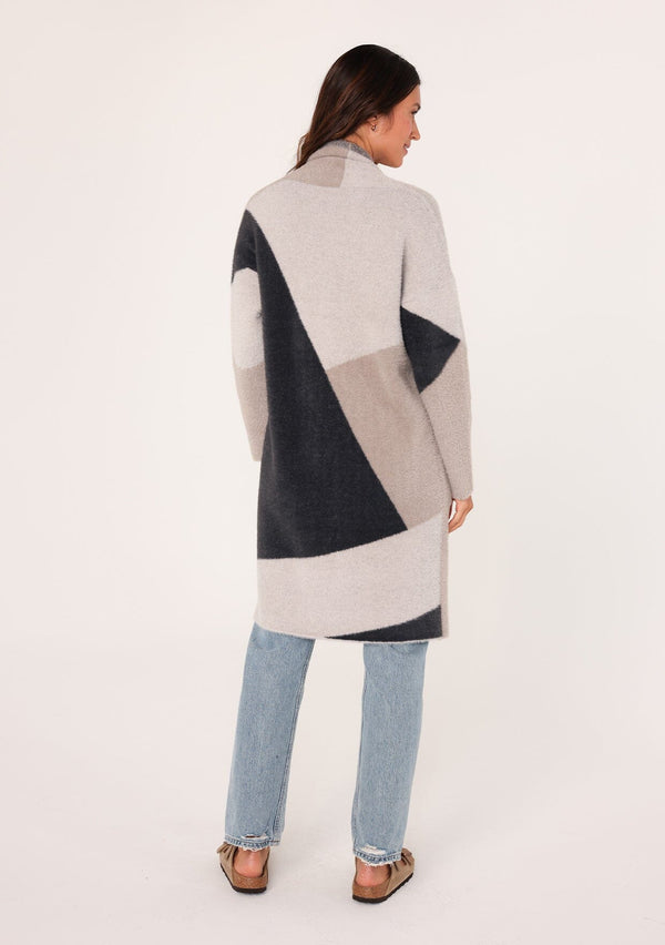 [Color: Grey/Charcoal] A back facing image of a brunette model wearing a soft and fuzzy mid length cardigan in a grey and taupe color block pattern. With an open front, long sleeves, and side pockets. 
