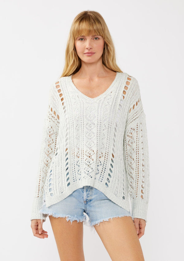[Color: Blue] A front facing image of a blonde model wearing a light blue open knit crochet pullover sweater with a v-neckline long sleeves, dropped shoulders, and a side vents. Designed for a relaxed look and fit for the spring season. 