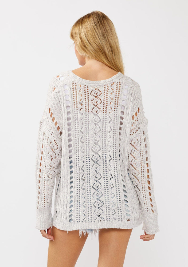 [Color: Lilac] A back facing image of a blonde model wearing a light purple open knit crochet pullover sweater with a v-neckline long sleeves, dropped shoulders, and a side vents. Designed for a relaxed look and fit for the spring season. 