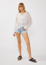 [Color: Lilac] A front facing image of a blonde model wearing a light purple open knit crochet pullover sweater with a v-neckline long sleeves, dropped shoulders, and a side vents. Designed for a relaxed look and fit for the spring season. 