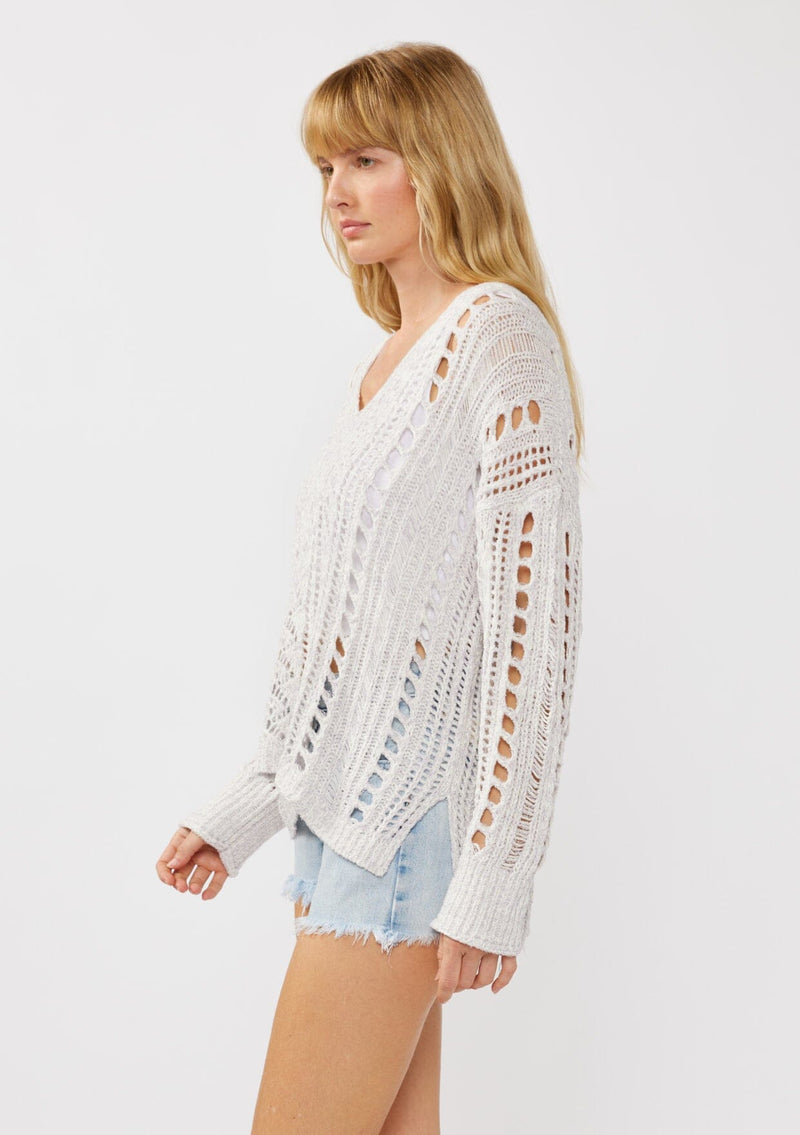 [Color: Lilac] A side facing image of a blonde model wearing a light purple open knit crochet pullover sweater with a v-neckline long sleeves, dropped shoulders, and a side vents. Designed for a relaxed look and fit for the spring season. 