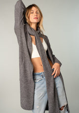 [Color: Olive] A model wearing a cozy dark grey long shawl cardigan. With long sleeves, side pockets, an open front, and attached scarf detail.