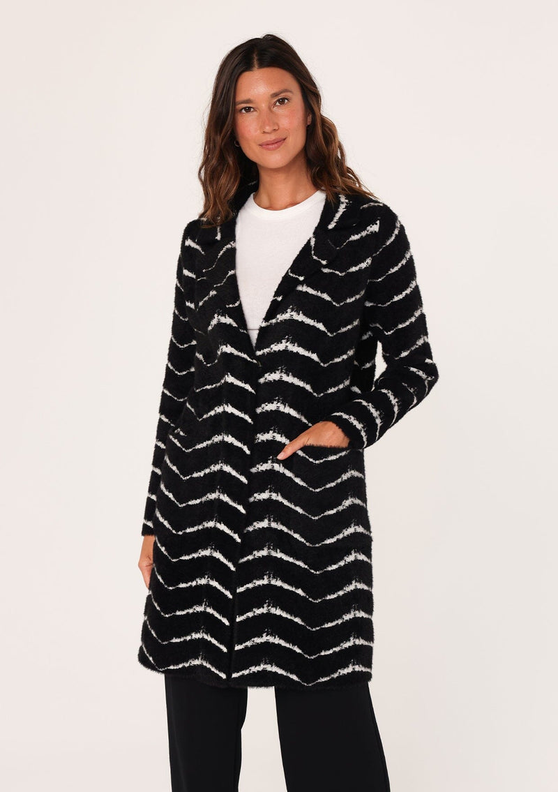 [Color: Black/White] A front facing image of a brunette model wearing a soft and fuzzy sweater coat in a black and white chevron design. With a snap button front, side pockets, and a classic notched lapel.