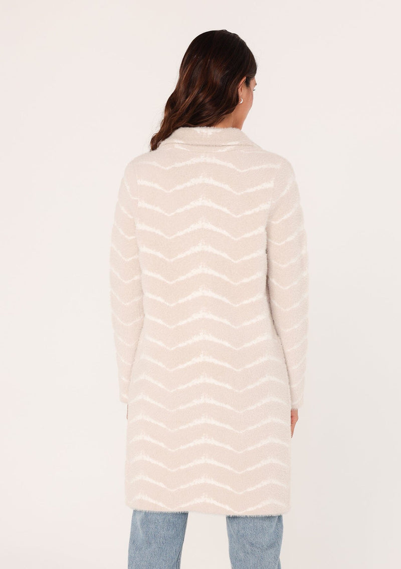 [Color: Sand/Cream] A back facing image of a brunette model wearing a soft and fuzzy sweater coat in an ivory and white chevron design. With a snap button front, side pockets, and a classic notched lapel.