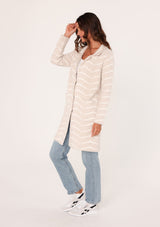 [Color: Sand/Cream] A side facing image of a brunette model wearing a soft and fuzzy sweater coat in an ivory and white chevron design. With a snap button front, side pockets, and a classic notched lapel.