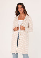 [Color: Sand/Cream] A front facing image of a brunette model wearing a soft and fuzzy sweater coat in an ivory and white chevron design. With a snap button front, side pockets, and a classic notched lapel.