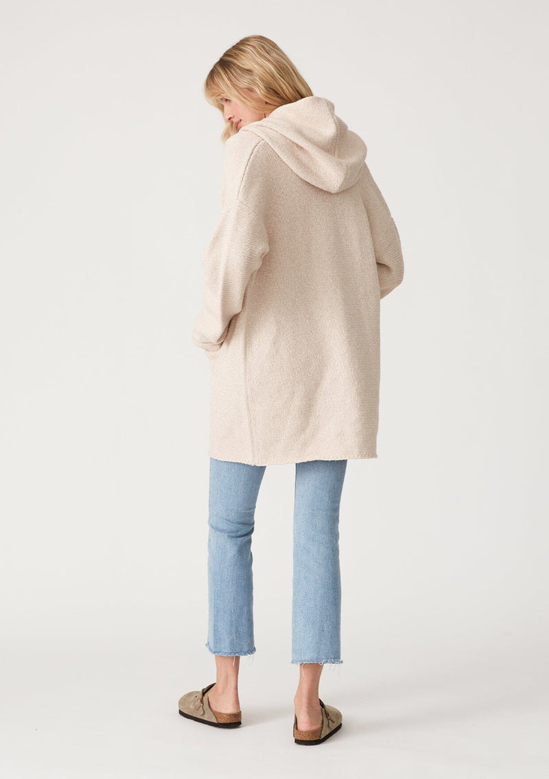 [Color: Heather Natural] A back facing image of a blonde model wearing an oversized sweater coat in ivory. With an oversized hood, long sleeves, an open front, side pockets, and a mid length. 