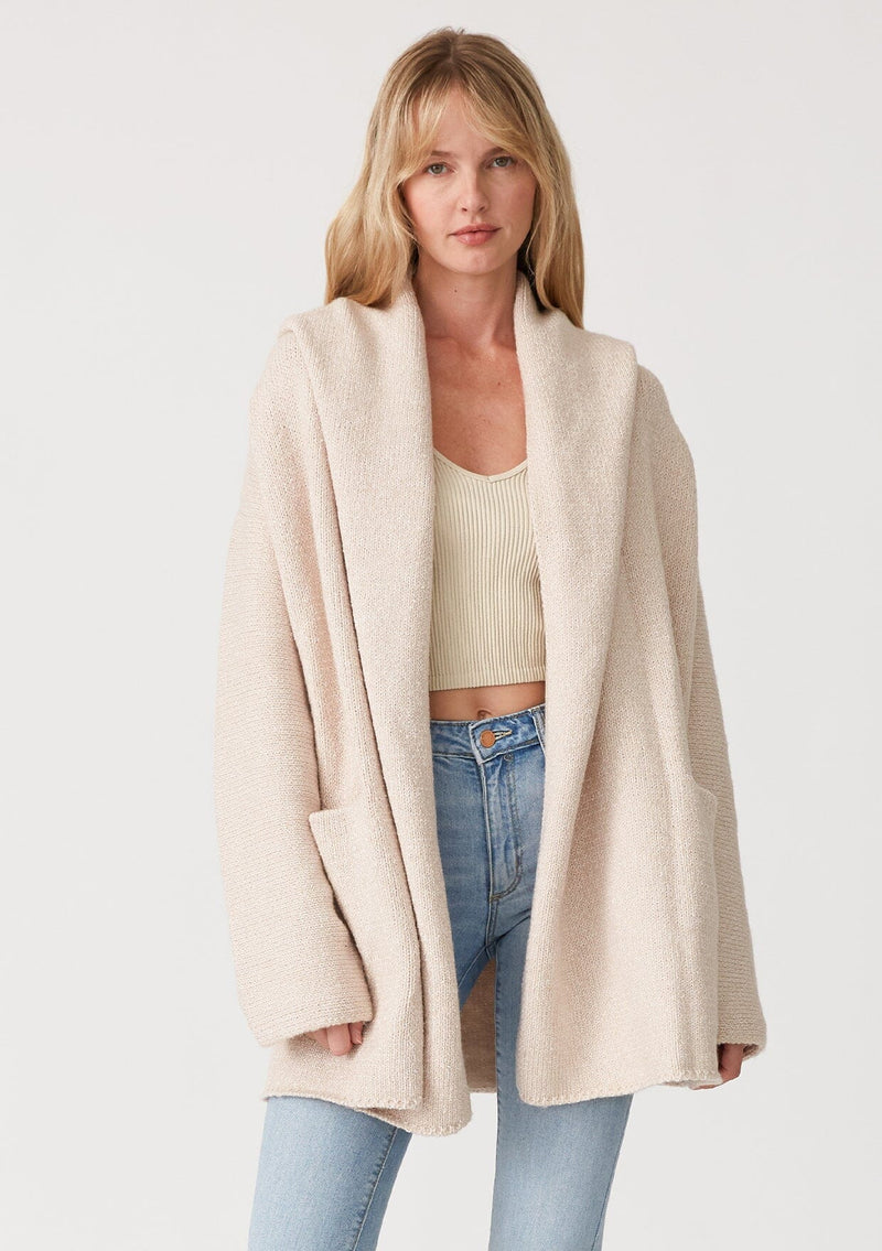 [Color: Heather Natural] A front facing image of a blonde model wearing an oversized sweater coat in ivory. With an oversized hood, long sleeves, an open front, side pockets, and a mid length. 
