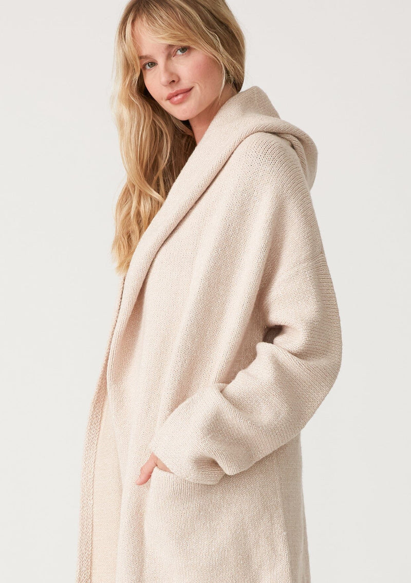 [Color: Heather Natural] A close up side facing image of a blonde model wearing an oversized sweater coat in ivory. With an oversized hood, long sleeves, an open front, side pockets, and a mid length. 