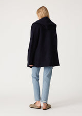 [Color: Navy] A back facing image of a blonde model wearing an oversized sweater coat in navy blue. With an oversized hood, long sleeves, an open front, side pockets, and a mid length. 