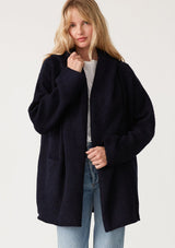 [Color: Navy] A half body front facing image of a blonde model wearing an oversized sweater coat in navy blue. With an oversized hood, long sleeves, an open front, side pockets, and a mid length. 
