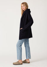 [Color: Navy] A side facing image of a blonde model wearing an oversized sweater coat in navy blue. With an oversized hood, long sleeves, an open front, side pockets, and a mid length. 