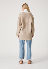 [Color: Natural] A back facing image of a blonde model wearing an oversize brown and ivory two tone knit cardigan. With an oversized shawl collar, an open front, and side pockets. 