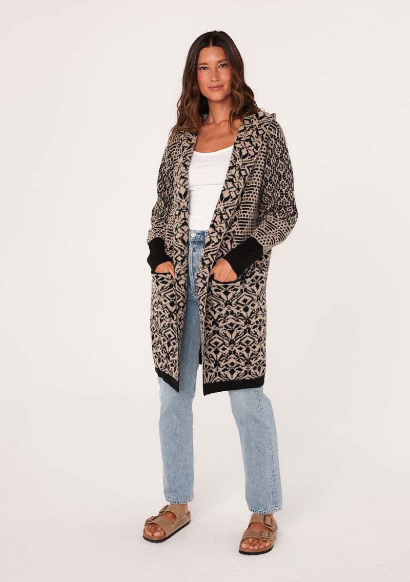 [Color: Taupe/Black] A full body front facing image of a brunette model wearing a soft boho cardigan in a brown and black abstract pattern. With a hoodie, an open front, a mid length hemline, and side pockets. 