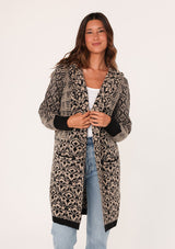 [Color: Taupe/Black] A front facing image of a brunette model wearing a soft boho cardigan in a brown and black abstract pattern. With a hoodie, an open front, a mid length hemline, and side pockets. 