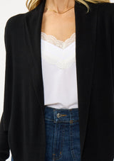 [Color: Black] A photo of a Lovestitch model wearing a chic black waffle knit wrap front sweater with long sleeves, a v neckline, and a button closure at the back. The long ties can be styled in multiple ways.