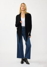 [Color: Black] A photo of a Lovestitch model wearing a chic black waffle knit wrap front sweater with long sleeves, a v neckline, and a button closure at the back. The long ties can be styled in multiple ways.