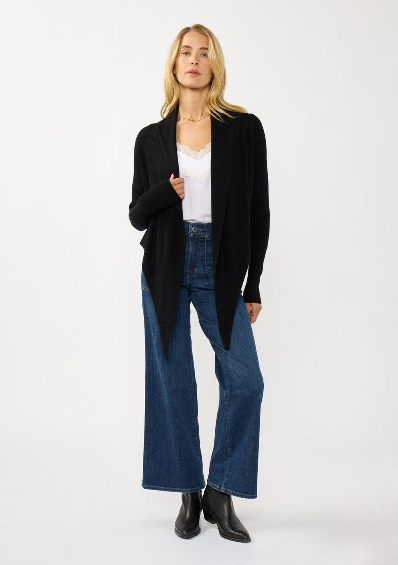 [Color: Black] A photo of a Lovestitch model wearing a chic black waffle knit wrap front sweater with long sleeves, a v neckline, and a button closure at the back. The long ties can be styled in multiple ways.