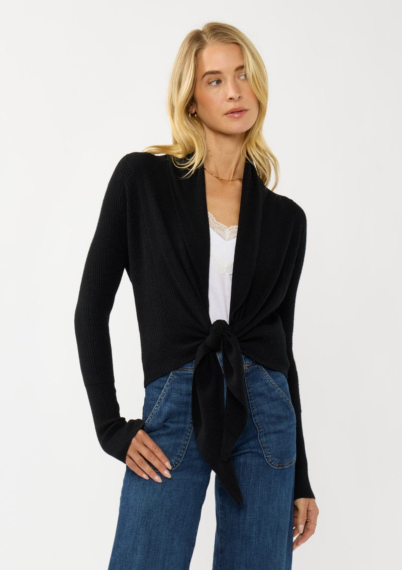 [Color: Black] A photo of a Lovestitch model wearing a chic black waffle knit wrap front sweater with long sleeves, a v neckline, and a button closure at the back. The long ties can be styled in multiple ways.