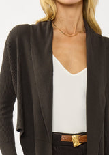 [Color: Dark Brown] A photo of a Lovestitch model wearing a chic brown waffle knit wrap front sweater with long sleeves, a v neckline, and a button closure at the back. The long ties can be styled in multiple ways.