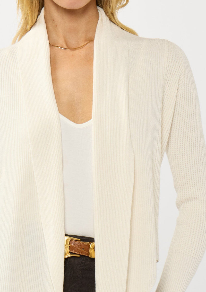 [Color: Natural] A photo of a Lovestitch model wearing a chic ivory waffle knit wrap front sweater with long sleeves, a v neckline, and a button closure at the back. The long ties can be styled in multiple ways.