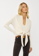 [Color: Natural] A photo of a Lovestitch model wearing a chic ivory waffle knit wrap front sweater with long sleeves, a v neckline, and a button closure at the back. The long ties can be styled in multiple ways.