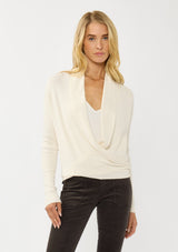 [Color: Natural] A photo of a Lovestitch model wearing a chic ivory waffle knit wrap front sweater with long sleeves, a v neckline, and a button closure at the back. The long ties can be styled in multiple ways.