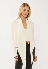 [Color: Natural] A photo of a Lovestitch model wearing a chic ivory waffle knit wrap front sweater with long sleeves, a v neckline, and a button closure at the back. The long ties can be styled in multiple ways.