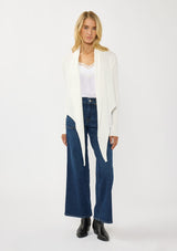 [Color: Winter White] A photo of a Lovestitch model wearing a chic white waffle knit wrap front sweater with long sleeves, a v neckline, and a button closure at the back. The long ties can be styled in multiple ways.