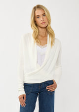 [Color: Winter White] A photo of a Lovestitch model wearing a chic white waffle knit wrap front sweater with long sleeves, a v neckline, and a button closure at the back. The long ties can be styled in multiple ways.