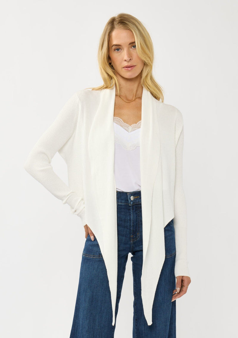 [Color: Winter White] A photo of a Lovestitch model wearing a chic white waffle knit wrap front sweater with long sleeves, a v neckline, and a button closure at the back. The long ties can be styled in multiple ways.
