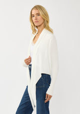 [Color: Winter White] A photo of a Lovestitch model wearing a chic white waffle knit wrap front sweater with long sleeves, a v neckline, and a button closure at the back. The long ties can be styled in multiple ways.