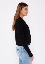 [Color: Black] A photo of a Lovestitch model wearing a chic black waffle knit wrap front sweater with long sleeves, a v neckline, and a button closure at the back. The long ties can be styled in multiple ways.