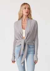 [Color: Heather Grey] A front facing image of a blonde model wearing a heather grey waffle knit wrap sweater with long sleeves, a v neckline, and a button closure at the back. The long ties can be styled in multiple ways. 