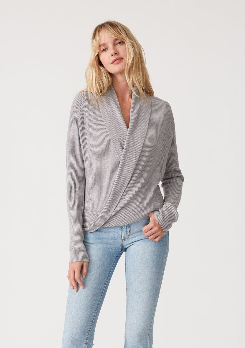 [Color: Heather Grey] A half body front facing image of a blonde model wearing a heather grey waffle knit wrap sweater with long sleeves, a v neckline, and a button closure at the back. The long ties can be styled in multiple ways. 