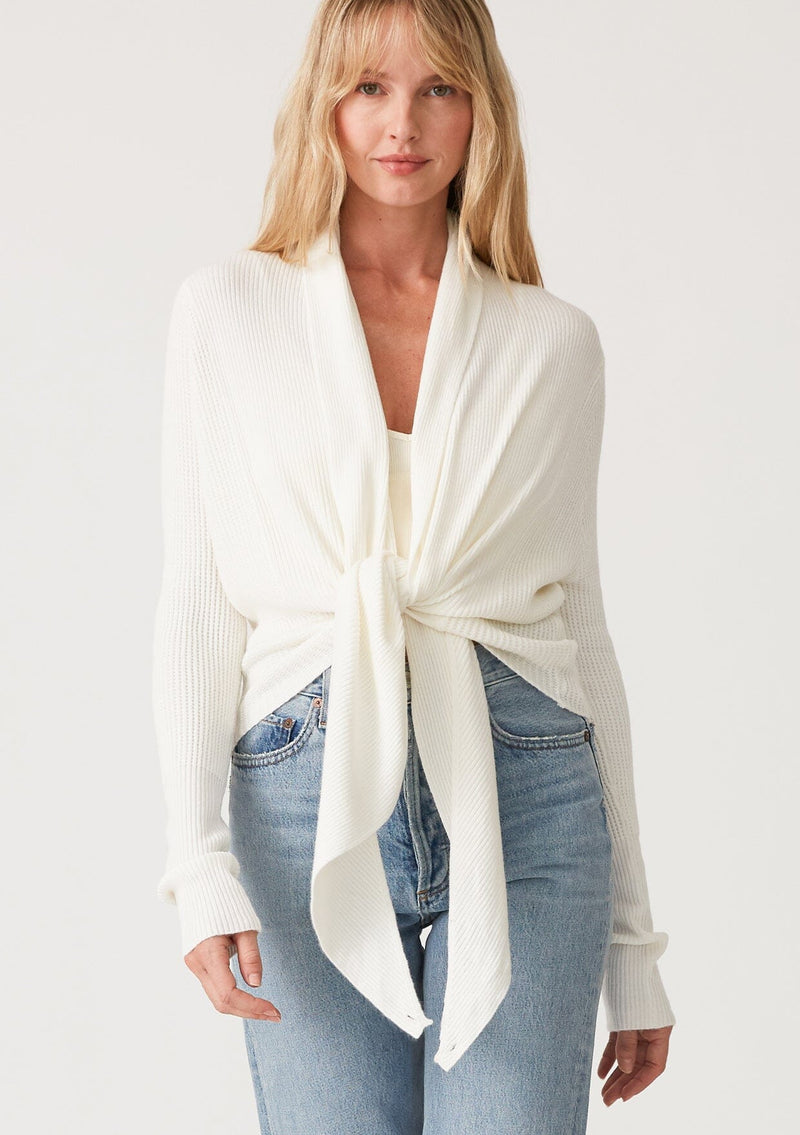 [Color: Ivory] A front facing image of a blonde model wearing an ivory waffle knit wrap sweater with long sleeves, a v neckline, and a button closure at the back. The long ties can be styled in multiple ways. 