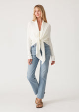 [Color: Ivory] A full body front facing image of a blonde model wearing an ivory waffle knit wrap sweater with long sleeves, a v neckline, and a button closure at the back. The long ties can be styled in multiple ways. 