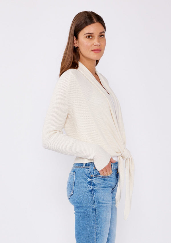 [Color: Natural] A photo of a Lovestitch model wearing a chic ivory waffle knit wrap front sweater with long sleeves, a v neckline, and a button closure at the back. The long ties can be styled in multiple ways.