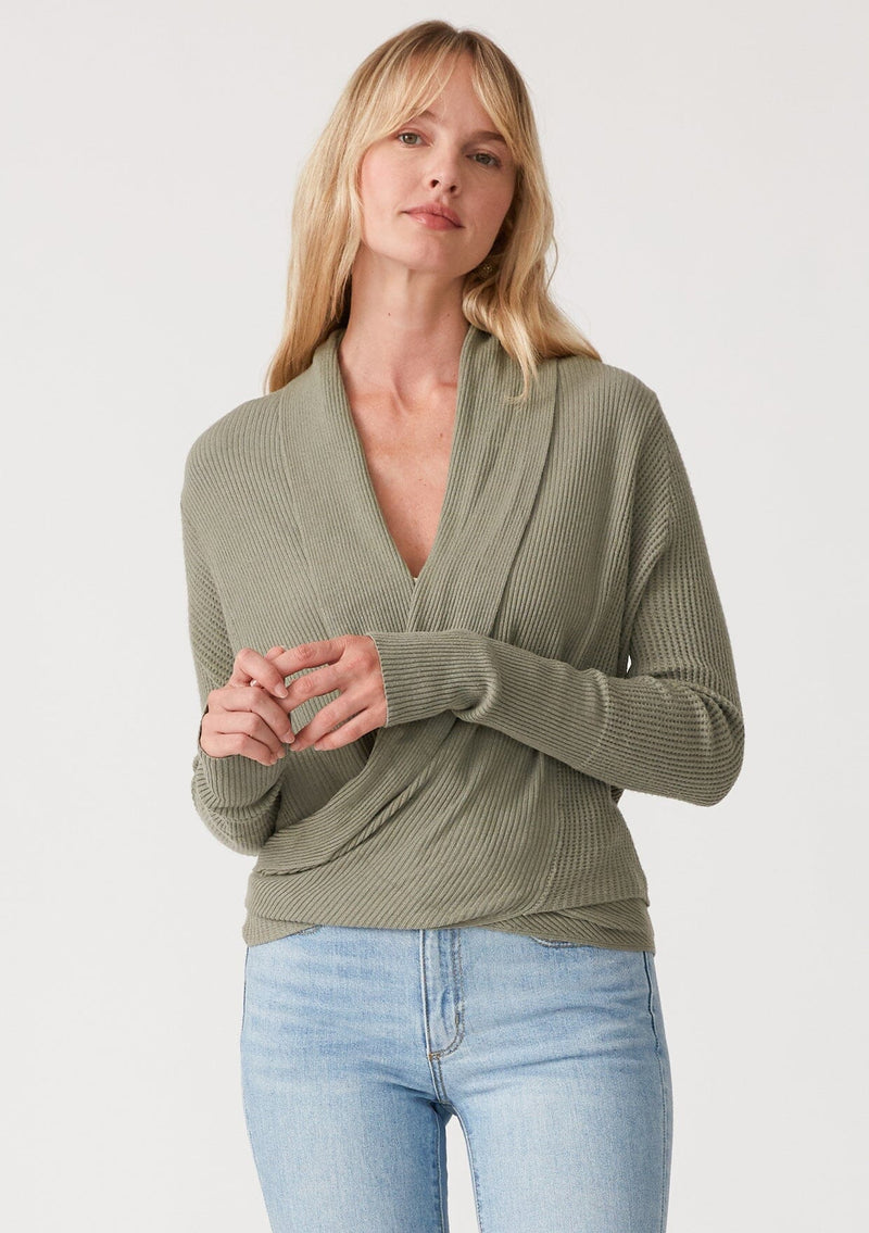 [Color: Olive] A front facing image of a blonde model wearing an olive green waffle knit wrap sweater with long sleeves, a v neckline, and a button closure at the back. The long ties can be styled in multiple ways. 