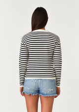 [Color: Cream/Black] A back facing image of a brunette model wearing a classic black and cream striped knit pullover sweater. With long sleeves, a drop shoulder, a crew neckline, and a twist front detail at the waist. 