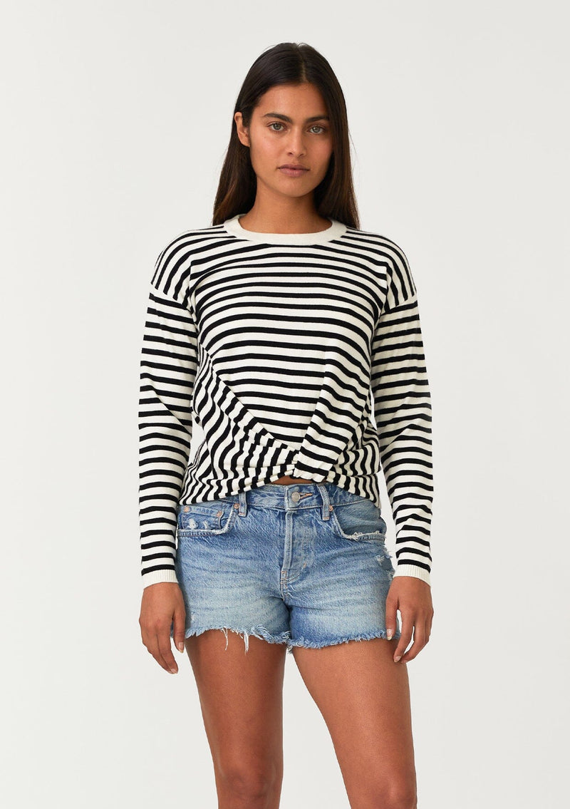 [Color: Cream/Black] A front facing image of a brunette model wearing a classic black and cream striped knit pullover sweater. With long sleeves, a drop shoulder, a crew neckline, and a twist front detail at the waist. 