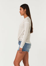 [Color: Ivory/Tan] A side facing image of a brunette model wearing a classic ivory and tan brown striped knit pullover sweater. With long sleeves, a drop shoulder, a crew neckline, and a twist front detail at the waist. 