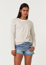 [Color: Ivory/Tan] A front facing image of a brunette model wearing a classic ivory and tan brown striped knit pullover sweater. With long sleeves, a drop shoulder, a crew neckline, and a twist front detail at the waist. 