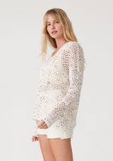 [Color: Ivory/Coral] A side facing image of a blonde model wearing a lightweight crochet hoodie in an ivory speckled knit. With long sleeves, a v neckline, a drawstring hoodie, and a dropped shoulder. 