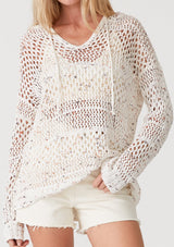 [Color: Ivory/Coral] A close up front facing image of a blonde model wearing a lightweight crochet hoodie in an ivory speckled knit. With long sleeves, a v neckline, a drawstring hoodie, and a dropped shoulder. 
