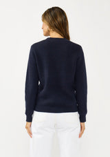 [Color: Navy] A back facing image of a brunette model wearing a classic crew neck sweater in navy blue. With ribbed trims, long sleeves, and a cable knit stitch detail. A versatile sweater perfect for layering.