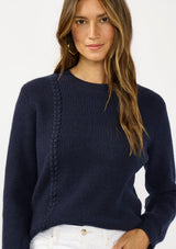 [Color: Navy] A brunette model wearing a classic crew neck sweater in navy blue. With ribbed trims, long sleeves, and a cable knit stitch detail. A versatile sweater perfect for layering.