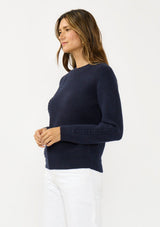[Color: Navy] A side facing image of a brunette model wearing a classic crew neck sweater in navy blue. With ribbed trims, long sleeves, and a cable knit stitch detail. A versatile sweater perfect for layering.