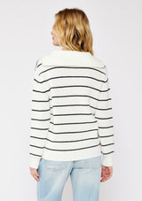 [Color: White/Black] A back facing image of a blonde model wearing a white and black striped knit pullover sweater with a half zip front. 