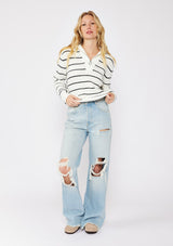 [Color: White/Black] A front facing image of a blonde model wearing a white and black striped knit pullover sweater with a half zip front. 